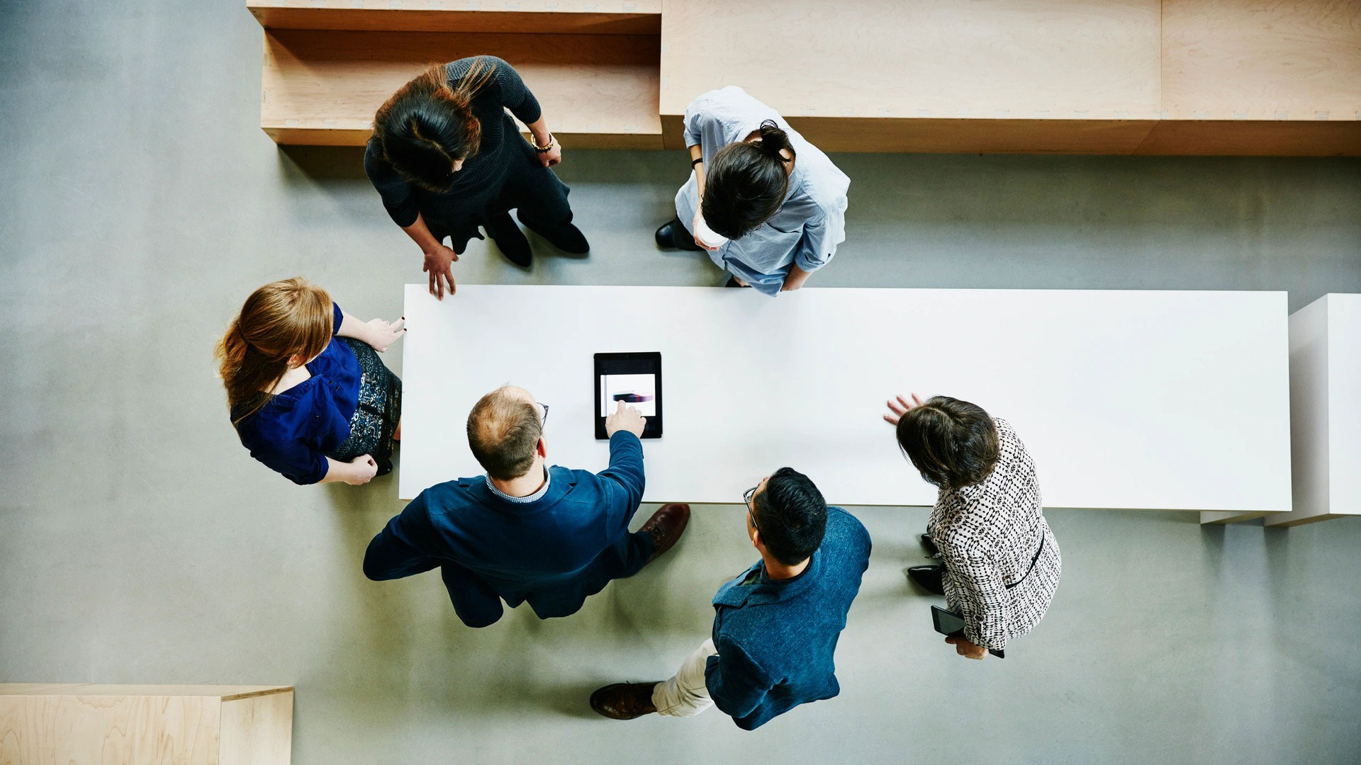 People standing around a table viewing a tablet viewed from above