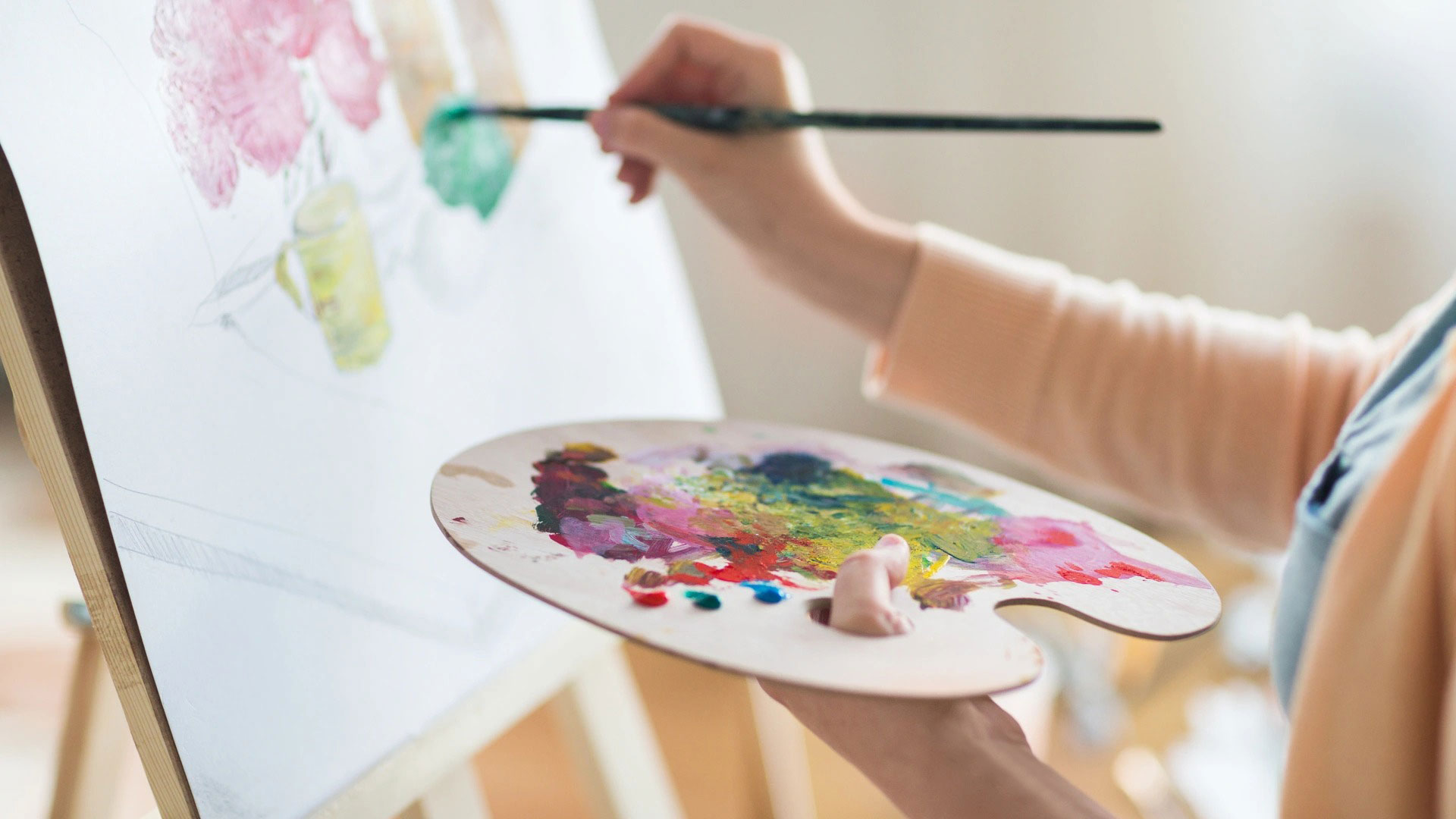 Person painting on an easel holding palette